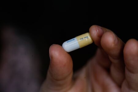 Bucharest, Romania - January 27, 2020:  Close up image with the the fingers of a little girl holding a Tamiflu capsule (oseltamivir), an antiviral medication that blocks the actions of influenza virus types A and B the human body.のeditorial素材