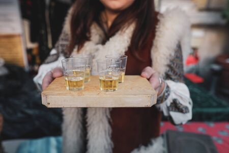 Shallow depth of field (selective focus) image with a woman holding a wooden plate with palinca (or tuica), romanian traditional plum brandy.の写真素材