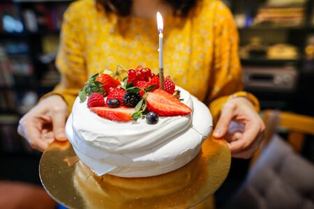 Shallow depth of field image (selective focus) with a woman holding a fresh fruits meringue cake with a lighted candle.の写真素材