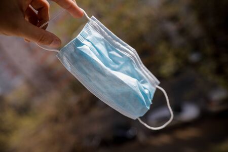 Shallow depth of field image (selective focus) with the hand of a man holding a nose and mouth medical mask.の写真素材
