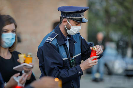 Bucharest, Romania - April 18, 2020: Romanian policeman with a surgical mask due to the covid-19 pandemic takes the Holy Light during the orthodox Easter.のeditorial素材