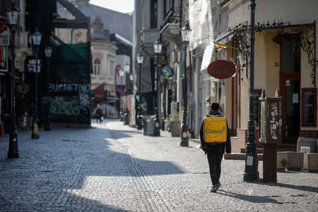 Bucharest, Romania - April 22, 2020: Man carrying a Glovo delivery backpack on the empty streets of Old Town Bucharest during the covid-19 lockdown.のeditorial素材