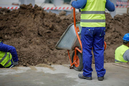 Bucharest, Romania - May 8, 2020: Details with a construction worker pushing a wheelbarrow on a construction site.のeditorial素材