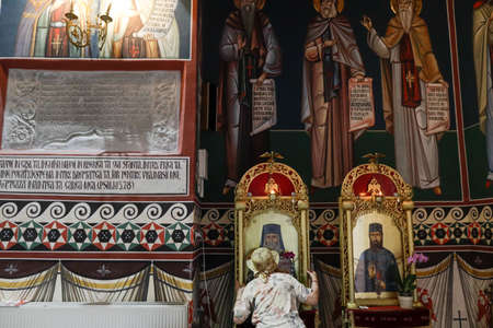 Snagov, Romania - June 21, 2020: Senior woman wearing a Covid-19 mask is praying outside a Orthodox Christian church.のeditorial素材