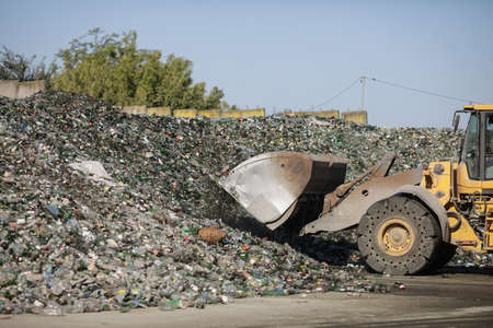 Bucharest, Romania - September 1, 2020: Earth mover operator arranging a pile of empty bottles in a...