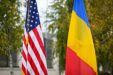 Shallow depth of field (selective focus) image with the US and Romanian flags on poles on a vegetal background.の写真素材
