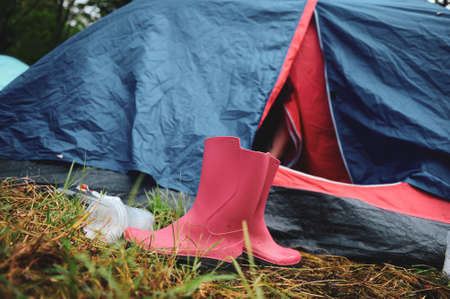 Details with pink rubber boots outside a tent in a camping area of a music festival during a rainy summer day.の写真素材