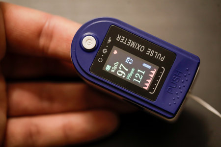 Details with the hand of a man measuring his pulse and blood oxygen level with a self use pulse oximeter at home during the Covid-19 outbreak.のeditorial素材