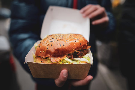 Shallow depth of field (selective focus) with the hands of a young man holding a boxed burger.の写真素材