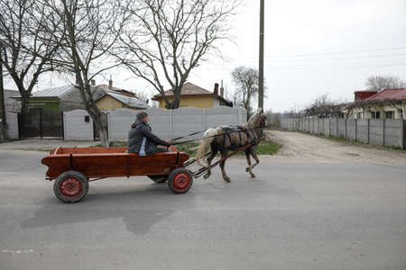 Sintesti, Romania - April 2, 2021: Man drives a horse drawn cart on a public road.のeditorial素材