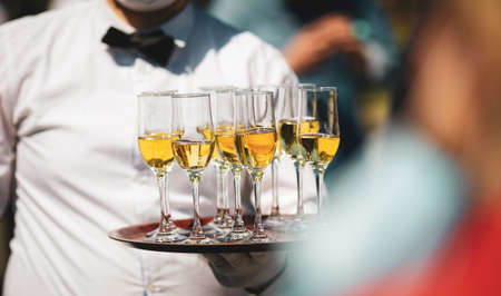 Shallow depth of field (selective focus) details with a waiter walking around and giving sparkling wine to the guests of an event.の写真素材