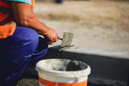 Shallow depth of field (selective focus) image with a worker cementing a sidewalk ledge on a construction site.の写真素材