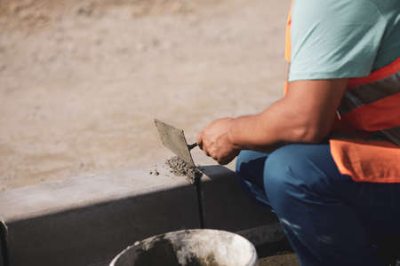 Shallow depth of field (selective focus) image with a worker cementing a sidewalk ledge on a construction site.の写真素材