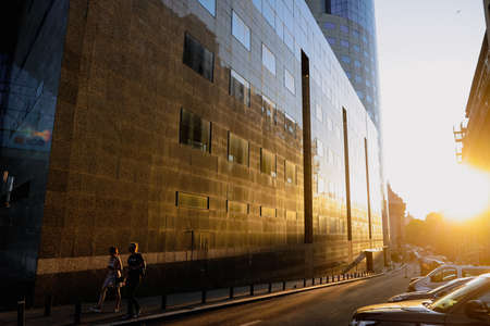 Bucharest, Romania - August 7, 2021: People walk near a tall glass office building at twilight in...