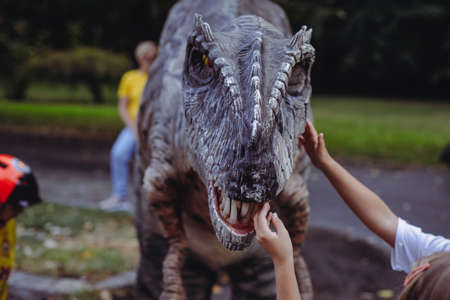 Bucharest, Romania - August 29, 2021: A man costumed as a carnivorous dinosaur walks between people and letâs them pet him during an outdoors event in Bucharest.のeditorial素材
