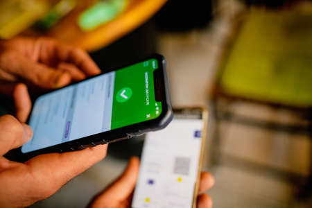 Bucharest, Romania - September 23, 2021: Shallow depth of field (selective focus) image with a restaurant client showing a Covid-19 certificate from a mobile phone to an employee.のeditorial素材