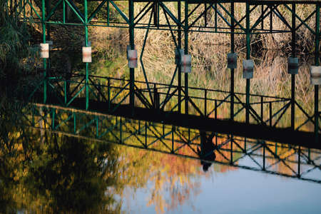 Reflection in water of people walking over a pedestrian bridge in a park during a sunny autumn day.の写真素材