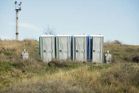 Portable public toilets in the middle of a field on a sunny winter day.