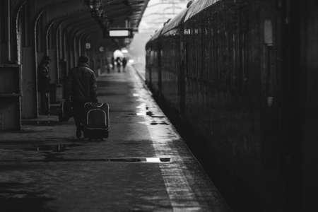 Black and white and (film noir, atmospheric) image with a man carrying a luggage near a train ready...