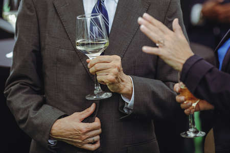 Details with a man and a woman interacting at a classy event, while holding  glasses of white wine.の写真素材