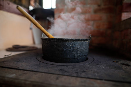 Cast iron cauldron boiling a goulash stew over a wood burning stove made from red bricks in the backyard of a rural house in Romania.の写真素材