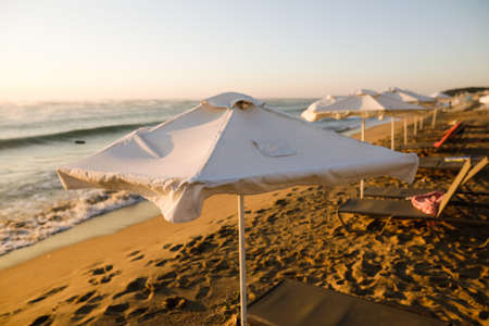 Lounge chairs and sun umbrellas on the beach on a calm and warm summer morning at the Black Sea in the Obzor resort in Bulgaria.の写真素材