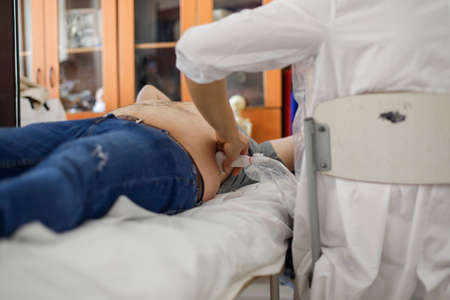 Details with the hands of a young medic making ultrasound investigations on the abdomen of a male...