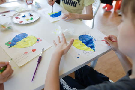Bucharest, Romania - May 9, 2022: Shallow depth of field (selective focus) details with Ukrainian refugee children drawing Ukrainian heart shaped flags.のeditorial素材
