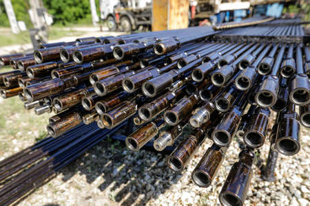 Oil rig drill pipes stacked with oil industry workers in the background. Oil and gas industry. Crude oil pump jack on an oil field. Drilling of oil and gas wells.の写真素材