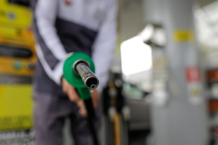 Shallow depth of field (selective focus) details with a man holding a fuel pump dripping with gasoline in a gas station.の写真素材