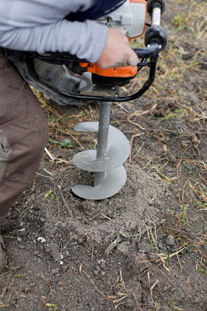 Shallow depth of field (selective focus) details with a man using a hand held earth hole drilling...