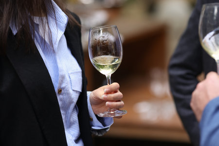 Shallow depth of field (selective focus) details with the hand of a woman holding a glass of white...