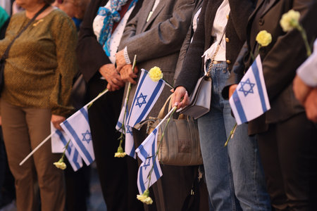 Details with the hands of a man holding the Israeli flag and a flower during a ceremony commemorating the October 2023 attacks.の写真素材