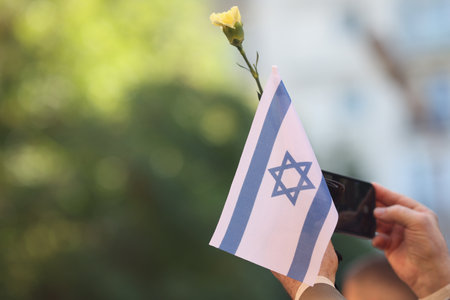 Details with the hands of a man holding the Israeli flag and a flower during a ceremony commemorating the October 2023 attacks.の写真素材