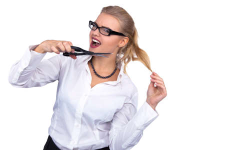 Angry businesswoman cutting her hair with scissors at office - Stock Image