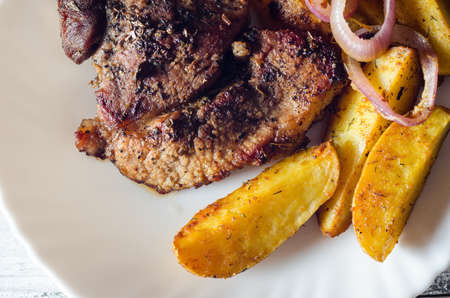 Grilled pork steaks with baked potatoes on plateの写真素材