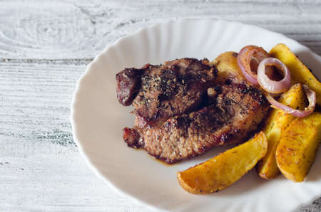 Grilled pork steaks with baked potatoes on plateの写真素材
