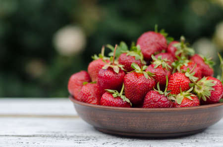 Ripe red strawberries on wooden table in clay plateの写真素材
