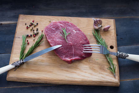 raw beef steak with rosemary and peppers on wooden boardの写真素材