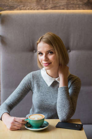 Woman drinking coffee in the morning at restaurant. Soft focus on the eyes. Sellphone on table.