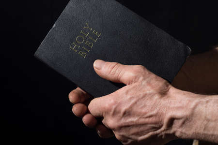 Aged man's hands holding the Bible. Black background.の写真素材