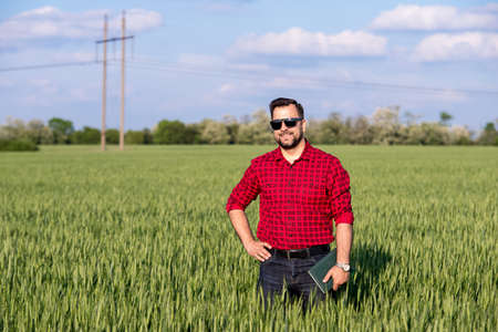 Young handsome farmer with diary standing in wheat fieldの写真素材