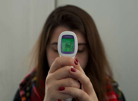 Close-up of hands of young woman checking herself her body temperature with a thermometer gun isometric medical digital. Measures to check fever and prevent the spread of COVID-19. Coronavirus conceptの写真素材