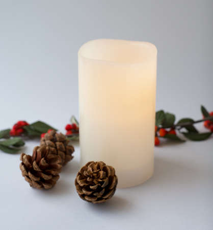 White christmas candle and christmas decoration on white background. Pine cones and red berries branch ornaments. Xmas objects. Selected focusの写真素材