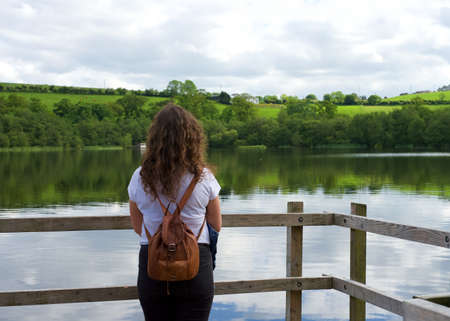 Young woman on her back sightseeing. Traveler discovering a landscape with a lake and green mountainsの写真素材