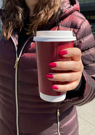 Young woman taking a coffee to go. Shades of red. Red nails, red coat and red cupの写真素材