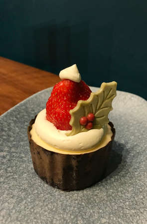 Dessert for the Christmas holidays. Cupcake with strawberry. Holly leaf and Santa Claus hatの写真素材