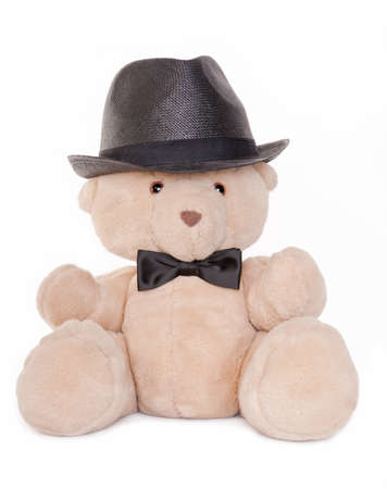 Sitting teddy bear wearing a bow tie and hat isolated on white