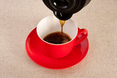 Hot expresso poured from a coffee pot into a red cupの写真素材