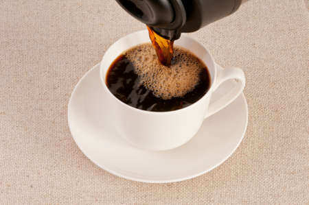 Hot black coffee from a coffee pot poured into a white cupの写真素材